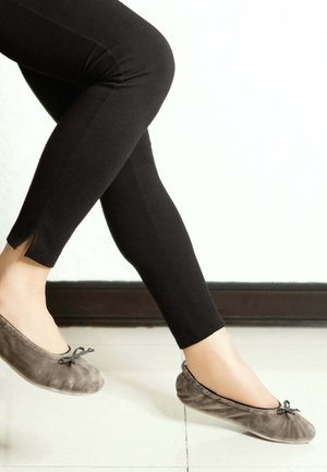 Leggings noirs avec une fente à la cheville, associés à des ballerines en daim gris avec un détail de nœud sur le bout. Texture lisse, design épuré.