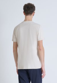 Camiseta de algodón beige con mangas cortas, cuello redondo y corte recto. Textura suave, sin patrones o gráficos visibles.