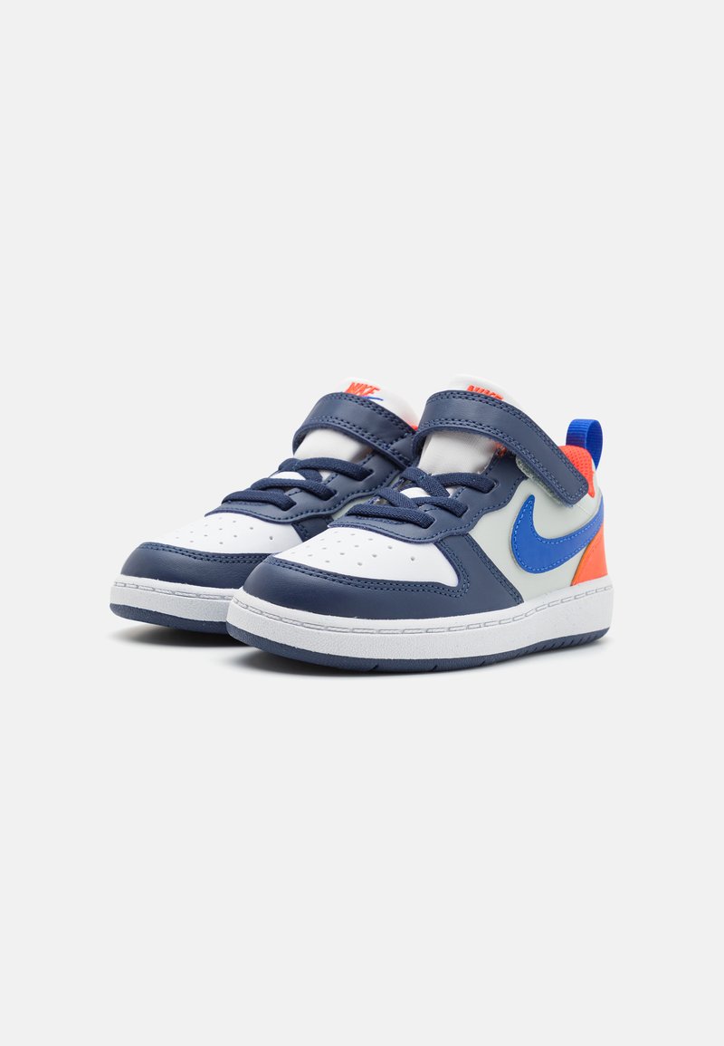 Marineblaue und weiße Sneaker mit einer Lederoberfläche, ausgestattet mit einem großen blauen Swoosh, orangefarbenen Akzenten und einem Klettverschluss über der Zunge.