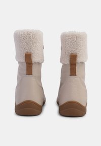 Beige enkellaarsjes met een fluffy witte nepbontmanchet, textuurmateriaal en een bruine rubberen zool. Voorzien van een trekband aan de achterkant voor eenvoudig aan- en uittrekken.