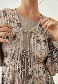 Blusa con estampado floral en tejido ligero, con escote fruncido y lazos. Presenta mangas abullonadas y una camiseta interior con capas y textura.