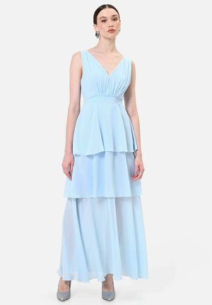 Femme portant une robe maxi à volants bleu clair sans manches avec un décolleté en V et une taille cintrée, associée à des talons hauts argentés et de grandes boucles d'oreilles.