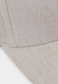 Gorra de color beige claro con una tela texturizada, visera curva, costuras visibles y un patrón sutil. El material parece transpirable y duradero.