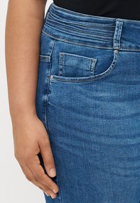 Saia de denim azul com uma superfície texturizada. Apresenta uma cintura alta, bolso lateral e detalhes de costura discretos.