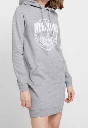 Kvinde iført en grå hættetrøjekjole med New York City skyline-grafik og kængurulomme.