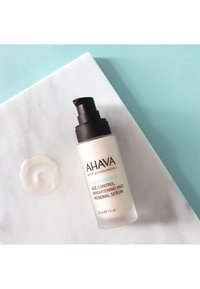 Siero AHAVA Time to Smooth in una bottiglia di vetro opalino con un erogatore scuro, etichettato per il controllo dell'età e il rinnovamento, accanto a un piccolo vortice di crema.
