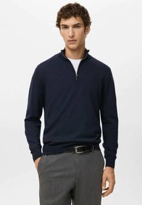 Granatowy sweter zapinany na suwak wykonany z dzianiny, z wysokim kołnierzem i długimi rękawami, zestawiony z szarymi spodniami dla uzyskania smukłego wyglądu.