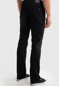Pantalones vaqueros de mezclilla negra con un diseño de pierna recta, que cuentan con bolsillos traseros y una etiqueta de logo en la cintura. Combinados con zapatillas negras.