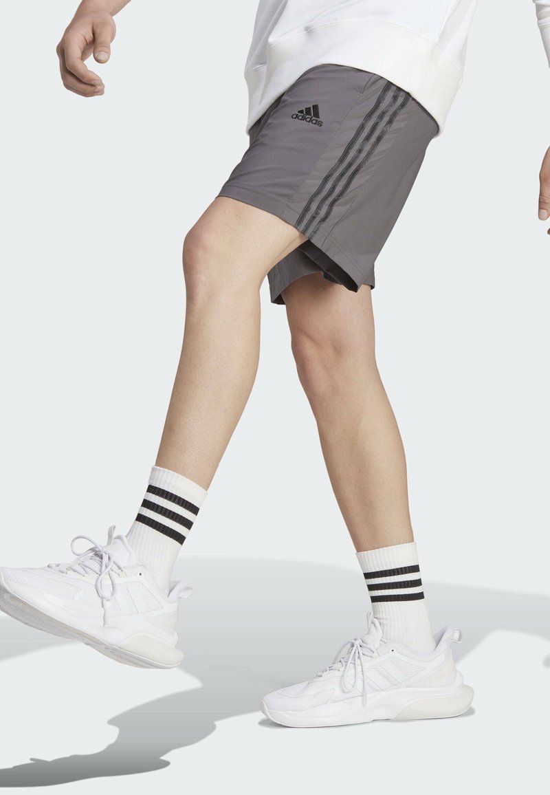 Grijze sportieve shorts met zwarte strepen, gecombineerd met witte schoenen en kniesokken met zwarte strepen. Casual, sportief ontwerp.