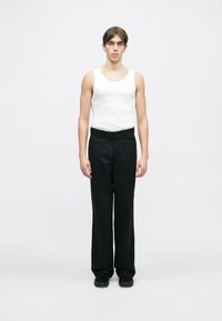 Hvit ermeløs tanktopp kombinert med svarte, vide bukser. Modellen står rett mot en ensfarget hvit bakgrunn. Svarte sko fullfører antrekket.