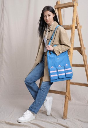 Blue canvas tote bag with three pink-striped pockets, featuring a top handle and an adjustable strap. Simple design with graphic accents.