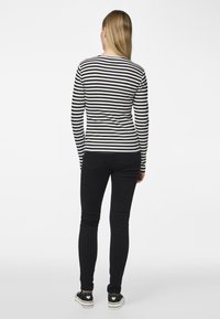 Zwart-wit gestreepte lange mouwen top, strakke pasvorm, geribbelde structuur, gecombineerd met zwarte skinny jeans en zwarte sneakers met hartaccenten.