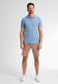 Ljusblå pikétröja i bomullstyg med en tvåknappsslå. Matchas med beige shorts och vita sneakers. Enkel, avslappnad design.