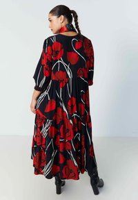 Zwarte maxi-jurk met rode bloemenprint en witte lijnen. Kenmerkt zich door een gelaagd ontwerp en lange mouwen. Draagt het met zwarte enkellaarsjes.