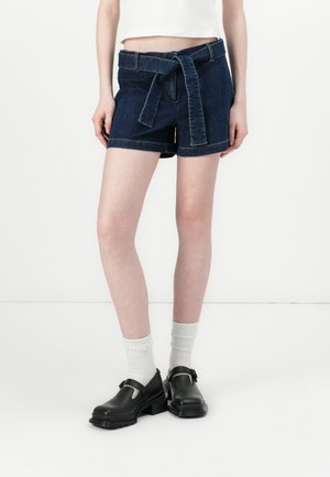 Mørkeblå denimshorts med knyttet belte, to frontlommer og rette ben. Kombinert med svarte sko og hvite sokker.