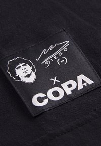 Sortt stofmærke med en hvid illustration af en persons ansigt, signatur ovenfor, og fed tekst der står "X COPA" forneden.