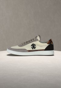 Άσπρο και γκρι sneaker χαμηλού ύψους με καφέ μοτίβο φίδιου δέρματος και μαύρο λογότυπο στο πλάι, τοποθετημένο σε ανοιχτή επιφάνεια.