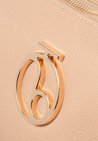 Borsa in pelle beige con superficie testurizzata, caratterizzata da un logo metallico prominente in oro, che mette in mostra curve dettagliate e linee eleganti.