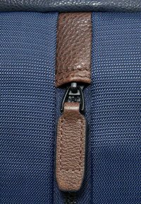 Borsa con cerniera in tessuto blu, caratterizzata da una linguetta in pelle marrone scuro, finitura testurizzata e resistente tirante della cerniera nero. Design chiaro e strutturato.