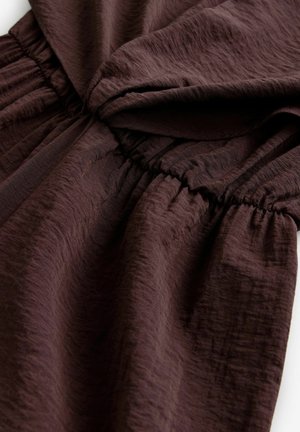 Brun tekstureret stof med et krøllet udseende, der har et elastisk samlede afsnit for pasform og flydende fald.