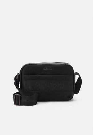Sac bandoulière rectangulaire noir Valentino avec bandoulière ajustable et détail du logo sur le devant, sur un fond clair uni.