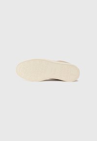 Suela de zapato en goma marrón con una superficie texturizada. Presenta patrones de huella circulares y un logo grabado en el lateral.