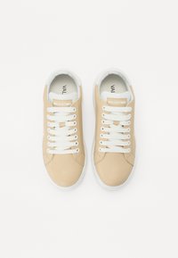 Lys beige sneakers med hvite lisser, med en glatt lærtekstur og logo detaljer på tungen, klassisk lavt design.