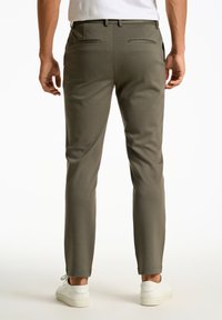 Pantalons vert olive foncé à coupe slim, avec deux poches arrière et une texture lisse, associés à des baskets blanches.