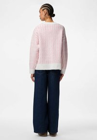 Oversized tröja i mjukt rosa och vitt med en texturerad, mönstrad design. Kombinerad med vida mörka denimjeans.
