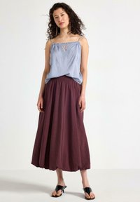 Lyseblå ærmeløs top med blonde detaljer, parret med en flydende burgunder maxi-nederdel. Sorte sandaler fuldender outfittet. Glatte teksturer er synlige.