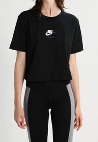 Černé kostkované tričko z bavlny s stříbrným logem Nike a textem "AIR" na přední straně. V páru s černými a šedými legínami.