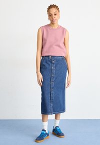 Top roz fără mâneci, fustă din denim cu talie înaltă și nasturi pe față, adidași albastri și negri, asortați cu șosete albe până la glezne. Texturi netede.