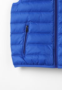 Blå puffväst i kviltad tyg, med en ficka med dragkedja och en framdragkedja. Slät textur och åtsittande design.