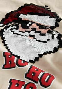 Arte in perline di Babbo Natale con cappello rosso e barba bianca su tessuto beige, con testo rosso e nero "HO HO HO" sottostante.