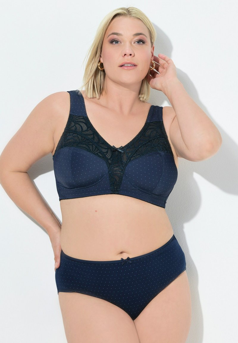 Navy blauwe lingerie set met een kanten beha met stippen en een strikaccent, gecombineerd met bijpassende bikini-stijl slips met stippen.