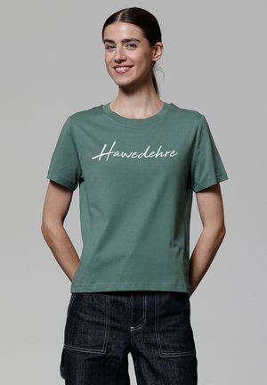 T-shirt en coton vert à manches courtes et col rond. Le devant présente un texte en cursive blanche "Hawedehre". Dos plain et coupe décontractée.