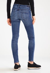 Tunna blå denimjeans med hög midja, försedd med två bakfickor och en slät textur. Matchas med svarta slip-on skor.