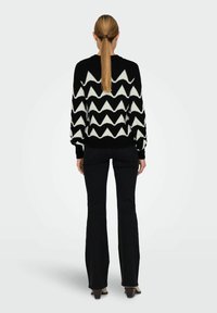 Maglione a maglia bianco e nero con motivo a zigzag, maniche lunghe, collo a girocollo e orlo a costine. Abbinato a pantaloni neri a palazzo.
