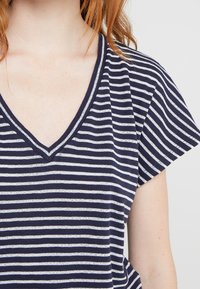 Marineblauw en witte gestreepte t-shirt met een V-hals en korte fladdermouwen. Zachte katoenen stof, comfortabele pasvorm en subtiele textuur in het materiaal.