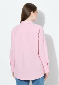 Camicia a maniche lunghe in rosa chiaro, realizzata in tessuto liscio, con piega posteriore, colletto appuntito e polsini con bottoni, abbinata a pantaloni in denim.