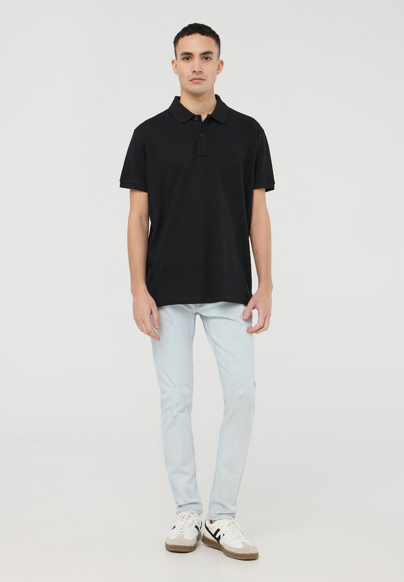 Polo shirt nera con maniche corte, abbinata a jeans strappati blu chiaro e sneakers bianche. Design semplice, senza loghi o motivi visibili.