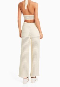Dwuczęściowy komplet na szydełku w kolorze kremowym, składający się z halterowego topu typu crop oraz szerokich spodni z teksturowanym splotem i otwartym wzorem oczek.