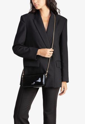 Bolso cruzado de charol negro con una correa de cadena dorada, textura suave, forma rectangular y un sutil detalle del logo en la parte frontal.