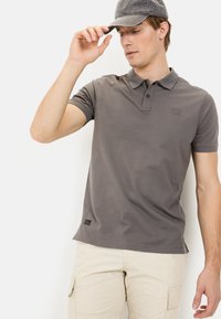 Grijze poloshirt met een kraag, twee knopen en een slim fit. Gestructureerde stof en een klein logo-embleem nabij de zoom. Gecombineerd met beige cargoshorts.