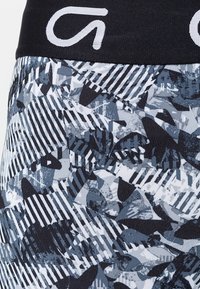 Leggings à motifs noir et gris présentant un mélange de formes abstraites et de rayures, fabriqués en tissu extensible avec une ceinture élastique noire.