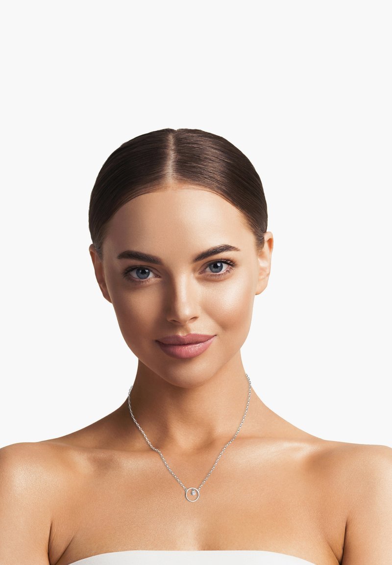 Sølv halskæde med en rund vedhæng, der har en delikat kæde. Modellen har skulderlangt hår og en neutral baggrund.