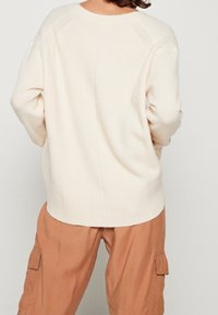 Maglione color crema in morbido tessuto, con orlo a coste e maniche raglan. Indossato con pantaloni cargo color marrone chiaro.