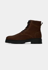 Stivale alla caviglia in suede marrone con lacci neri, suola in gomma e dettagli di cucitura. Presenta una linguetta posteriore per una facile calzata.