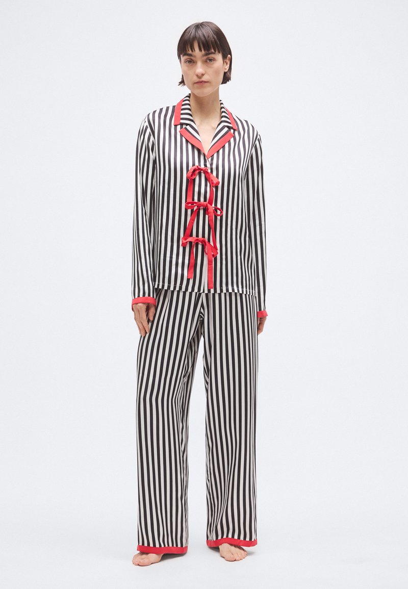 Set de pijama cu dungi, având dungi verticale alb-negru, accente roșii și închideri cu panglică pe cămașă, realizat dintr-un material neted.