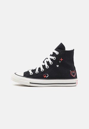 Zapatillas altas negras de lona, con cordones blancos, suela de goma blanca y patrones decorativos de corazones en rojo y blanco.